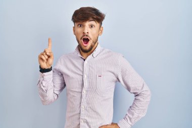 Mavi arka planda duran sakallı bir Arap başarılı bir fikir işaret ediyor. Heyecanlı ve mutlu. Bir numara.. 