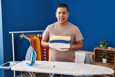 İspanyol genç adam ütüledikten sonra katlanmış çamaşırları tutuyor komik bir ifadeyle dilini dışarı çıkarıyor.. 