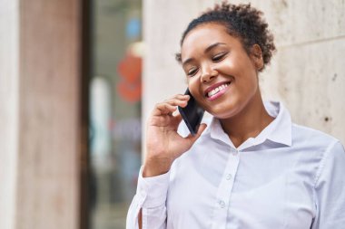 Afro-Amerikalı kadın gülümsüyor. Akıllı telefondan konuşuyor.