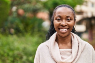 Afro-Amerikalı kadın parkta kendinden emin bir şekilde gülümsüyor.