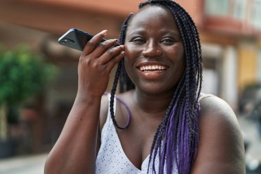 Afro-Amerikalı kadın gülümsüyor. Kafe terasındaki akıllı telefonun kendine güvenen sesli mesajını dinliyor.