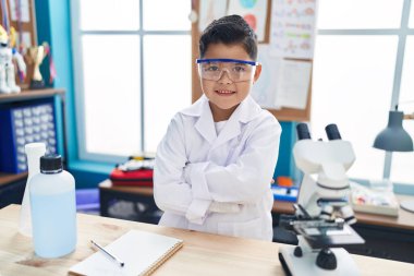 Sevimli İspanyol çocuk gülümsüyor. Kollarını kavuşturup laboratuvar sınıfına gidiyor.