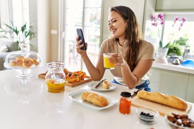 Genç ve güzel İspanyol kadın kahvaltısını mutfakta akıllı telefon kullanarak yapıyor.