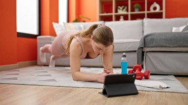 Genç sarışın kadın evde online vücut egzersizi yapıyor.