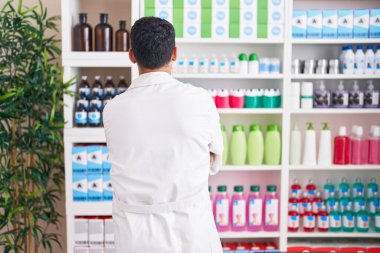 Eczanede çalışan yakışıklı İspanyol adam arkasını dönüp kollarını kavuşturmuş bakıyor. 
