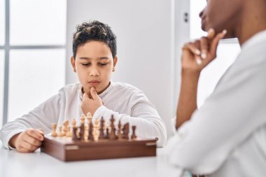 Afro-Amerikan anne ve oğlu evdeki masada oturmuş satranç oynuyorlar.