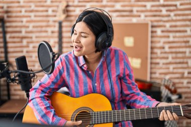 Young chinese woman musician playing guitar at music studio
