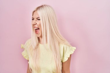 Pembe arka planda duran beyaz bir kadın kızgın ve kızgın çığlık atıyor ve öfkeden köpürüyor. Öfkeyle bağırıyor. öfke ve agresif konsept. 