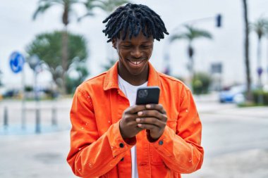 Sokakta akıllı telefon kullanan, kendinden emin gülümseyen Afrikalı Amerikalı bir adam.