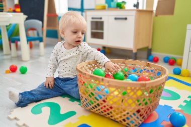 Anaokulunda yerde taşaklarıyla oynayan sevimli sarışın çocuk.