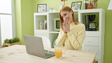 Young blonde woman using laptop having breakfast at home