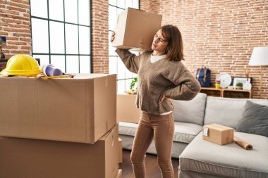 Young caucasian woman with backache holding package at new home