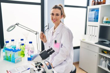 Young woman wearing scientist uniform holding glasses at laboratory