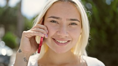 Genç, güzel İspanyol kadın gülümsüyor. Parktaki akıllı telefondan konuşuyor.