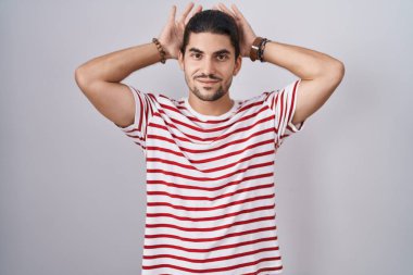 Uzun saçlı İspanyol bir adam izole edilmiş arka planda duruyor. Avuçlarında alaycı ve şüpheci bakışlarla tavşan kulağı hareketi yapıyor. Paskalya tavşanı konsepti. 