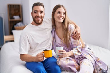 Man and woman couple hugging each other drinking coffee at bedroom