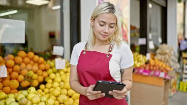 Genç ve güzel İspanyol kadın önlük giyiyor. Meyve dükkanında dokunmatik ped kullanıyor.
