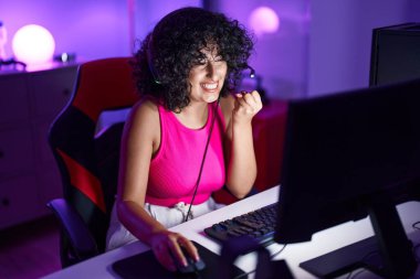Young middle eastern woman streamer playing video game using computer at gaming room