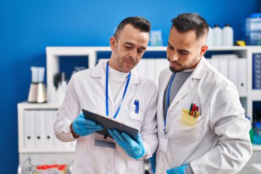 Two men scientists reading document with relaxed expression at laboratory
