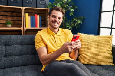 Evdeki kanepede oturan, akıllı telefon kullanan genç bir İspanyol.