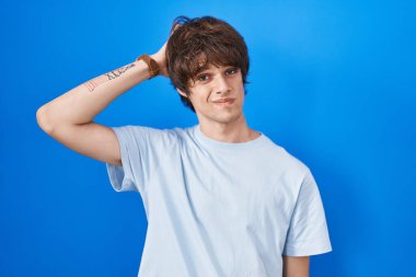 Mavi arka planda duran İspanyol genç adamın kafası karışmış ve soru sormayı merak ediyor. Şüpheyle kararsız, kafa kafaya düşünerek. Düşünceli kavram. 