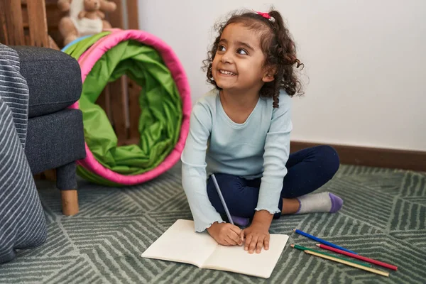 stock image Adorable hispanic girl drawing on notebook sitting on floor at home