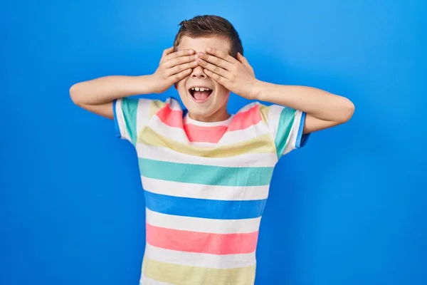 stock image Young caucasian kid standing over blue background covering eyes with hands smiling cheerful and funny. blind concept. 