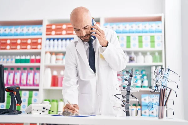 Young Bald Man Pharmacist Talking Smartphone Writing Document Pharmacy — Foto de Stock
