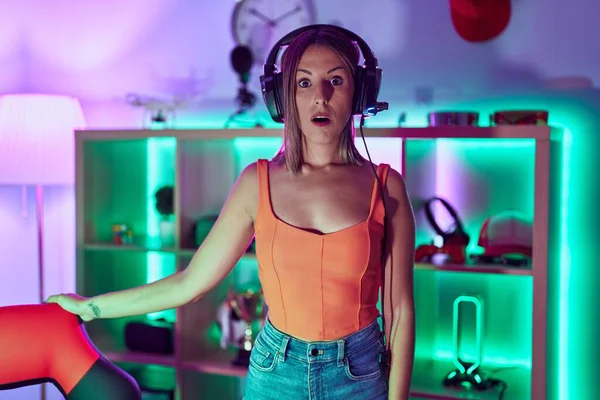 stock image Young woman playing video games wearing headphones scared and amazed with open mouth for surprise, disbelief face 