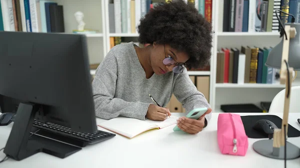 アフリカ系アメリカ人の女子学生が図書館大学のノートにスマホで書く — ストック写真