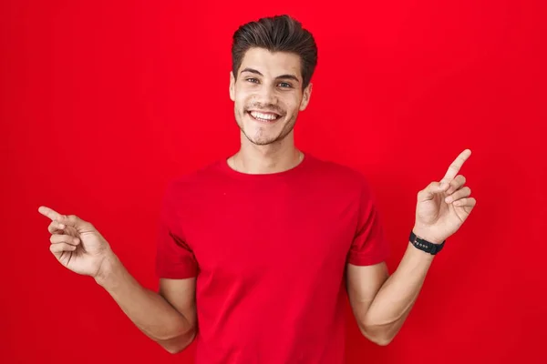Mladý Hispánec Stojící Nad Červeným Pozadím Sebevědomě Usmívá Ukazuje Prsty — Stock fotografie