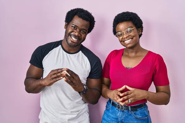 年轻的非洲裔美国夫妇手挽手站在粉红的背景上 手指交叉在一起 微笑着放松而快乐 成功与乐观 — 图库照片