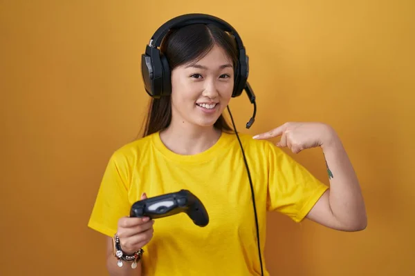 中国的年轻女子一边玩电子游戏一边带着自信的样子 脸上挂着微笑 用手指指着自己 既自豪又快乐 — 图库照片