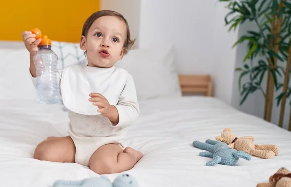 stock image Adorable hispanic boy sitting on bed holding bottle of water at bedroom