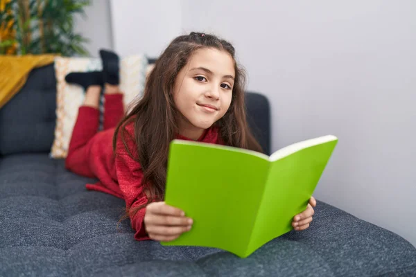 Adorable Hispanic Girl Reading Book Lying Sofa Home — Fotografia de Stock