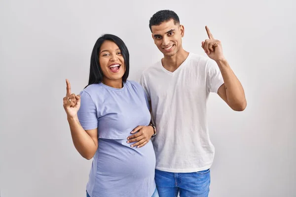 Jovem Casal Hispânico Esperando Bebê Sobre Fundo Sorrindo Espantado Surpreso — Fotografia de Stock