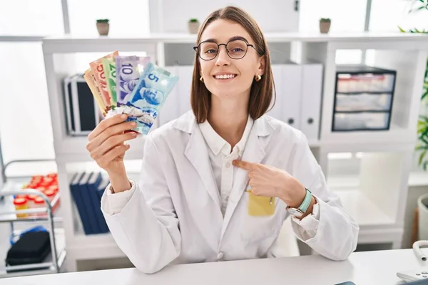 Młoda Kaukaska Lekarz Kobieta Trzyma Kanadyjskie Dolary Banknoty Wskazując Palcem — Zdjęcie stockowe