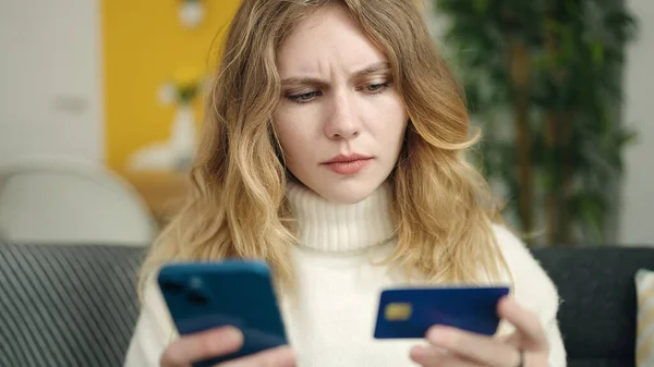 Młoda Blondynka Pomocą Smartfona Karty Kredytowej Siedzi Kanapie Domu — Zdjęcie stockowe