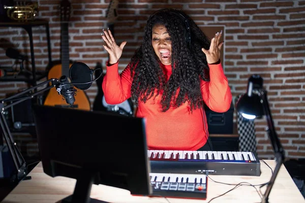 stock image Plus size hispanic woman playing piano at music studio celebrating crazy and amazed for success with arms raised and open eyes screaming excited. winner concept 