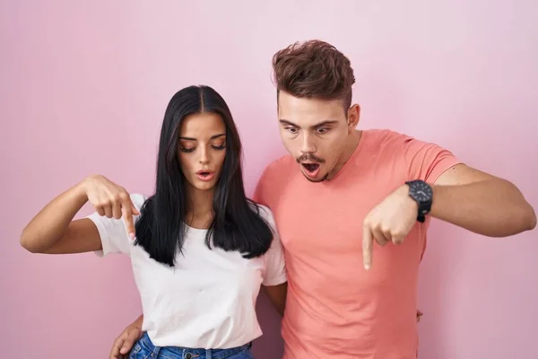 Молодая Латиноамериканская Пара Стоящая Розовом Фоне Указывая Пальцами Рекламу Удивленное — стоковое фото
