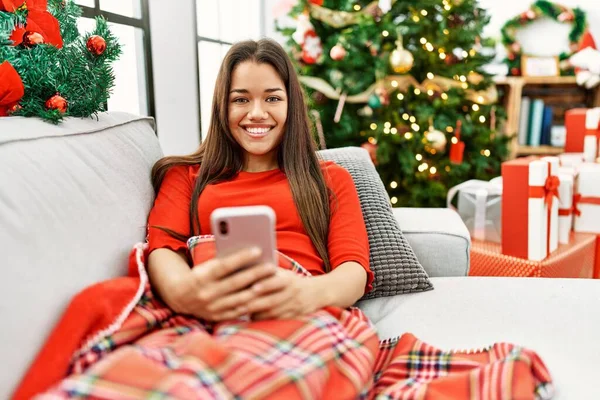 Νεαρή Λατίνα Γυναίκα Που Χρησιμοποιεί Smartphone Κάθεται Από Χριστουγεννιάτικο Δέντρο — Φωτογραφία Αρχείου