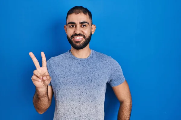 自信と幸せな笑顔ながら 青の背景に立っている髭を生やした中東の男は 指の数2を示すと指摘します — ストック写真