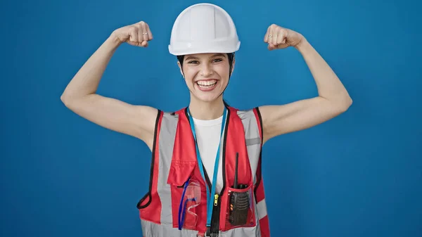 惊慌失措的女建筑工人微笑着 自信地在孤独的蓝色背景下做着强有力的手势 — 图库照片