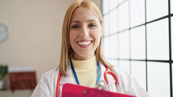 年轻的金发女医生微笑着 自信地在诊所拿着剪贴板 — 图库照片