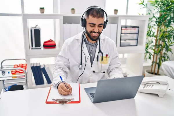 Young Hispanic Man Doctor Listening Music Writing Medical Report Clinic — Zdjęcie stockowe