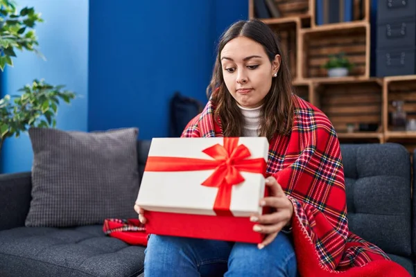 Young hispanic woman opening gift box skeptic and nervous, frowning upset because of problem. negative person.