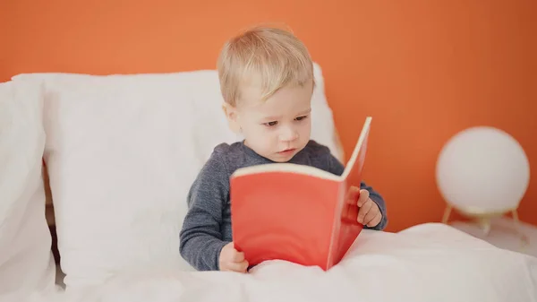 可愛いですブロンド幼児読書ストーリー本座っています上のベッドルーム — ストック写真