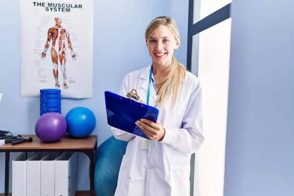 stock image Young blonde woman wearing physiotherpist uniform writing on checklist at physiotherapy clinic