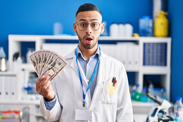 怖いお金を持っている科学研究所で働いている若いヒスパニック系の男と驚きのために口を開けて驚いて 不信の顔 — ストック写真