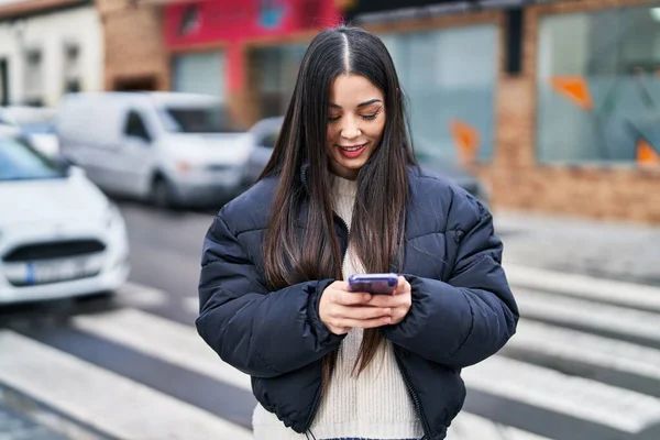 Genç, güzel, İspanyol bir kadın sokakta akıllı telefon kullanarak gülümsüyor.